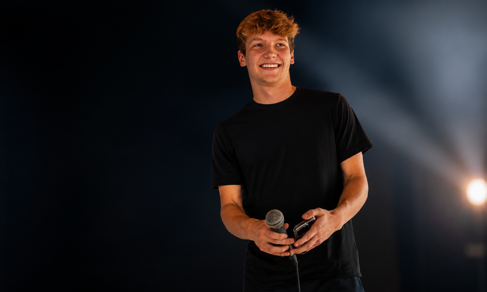 Elijah Parks smiling on stage holding a microphone under a spotlight